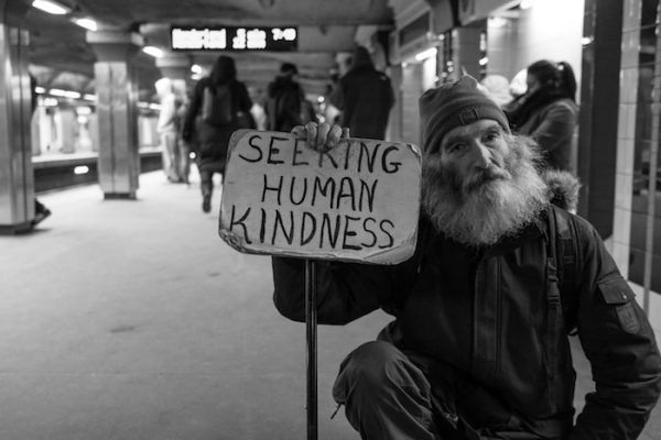 Bearded Man holds up cardboard sign Seeking Human Kindness