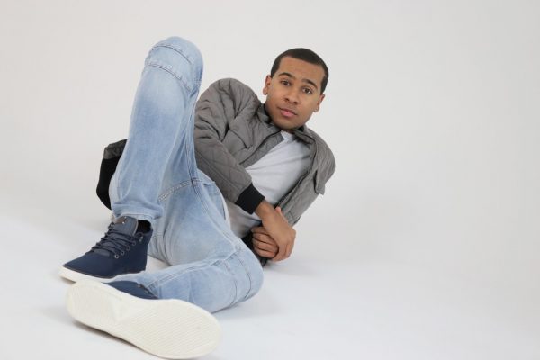 Anthony Brown in jeans, t-shirt and jacket reclining on floor