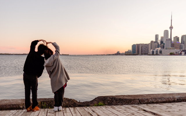A cute couple makes a heart with their arms while overlooking the Toronto skyline