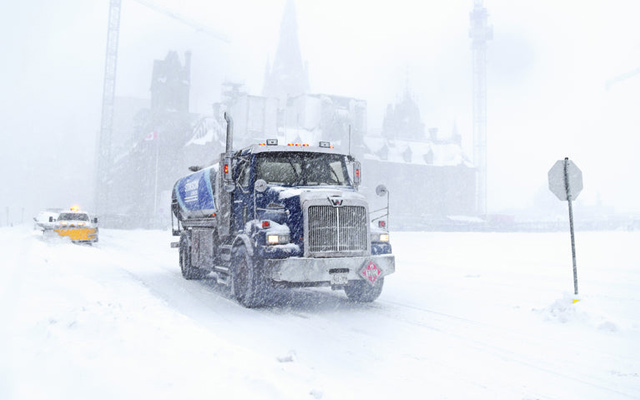 a blue Western Star tanker truck navigates a snowy road in the winter